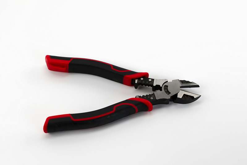 Close-up of high-quality insulated lineman's pliers and precision needle-nose pliers arranged neatly on a clean workbench next to insulated wire and a multimeter